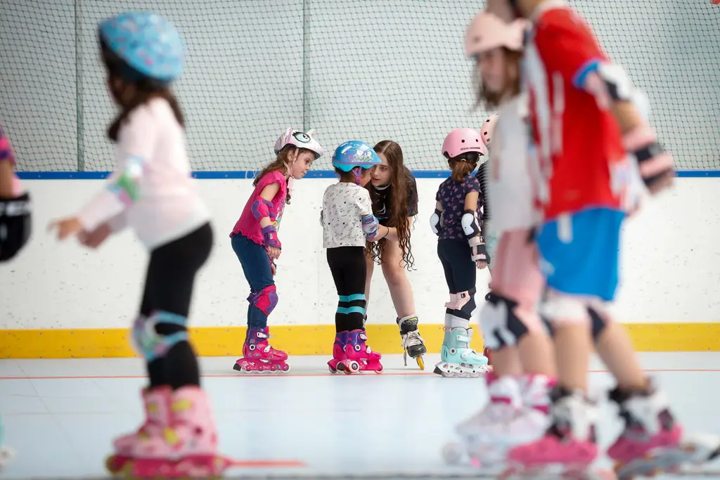 Una monitora de la escuela agachada entre un grupo de peques con casco y patines