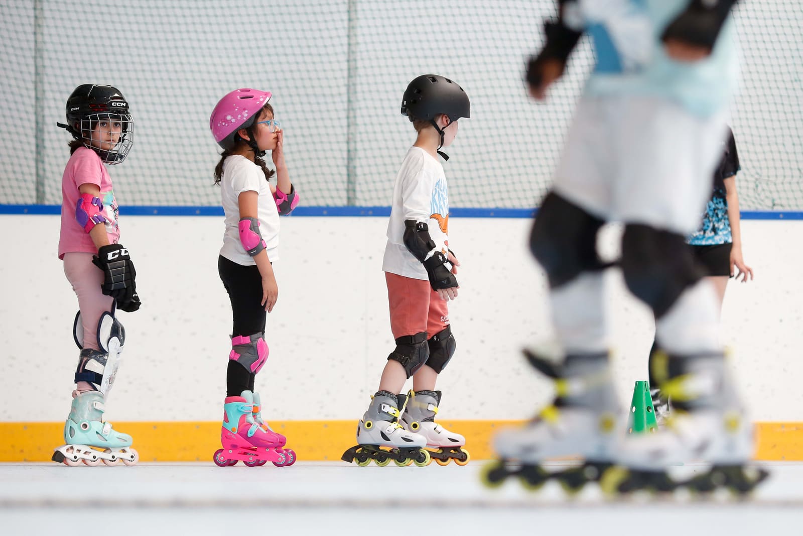 Fila de peques apoyados en la valla, con los patines puestos