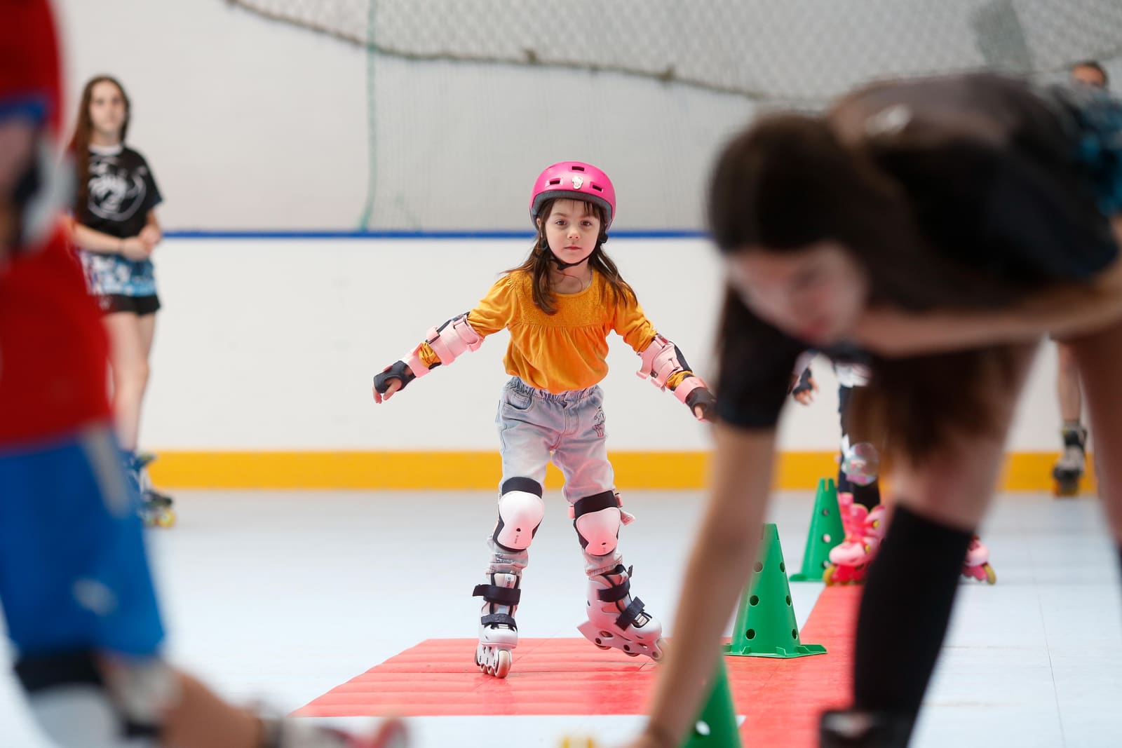 Una peque de la escuela patinando entre conos con casco y protecciones